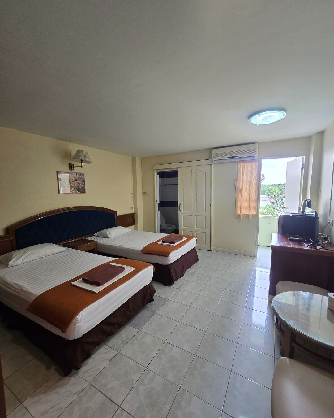 Een hotelkamer met twee bedden, een bureau met stoel, een televisie en een airconditioning.