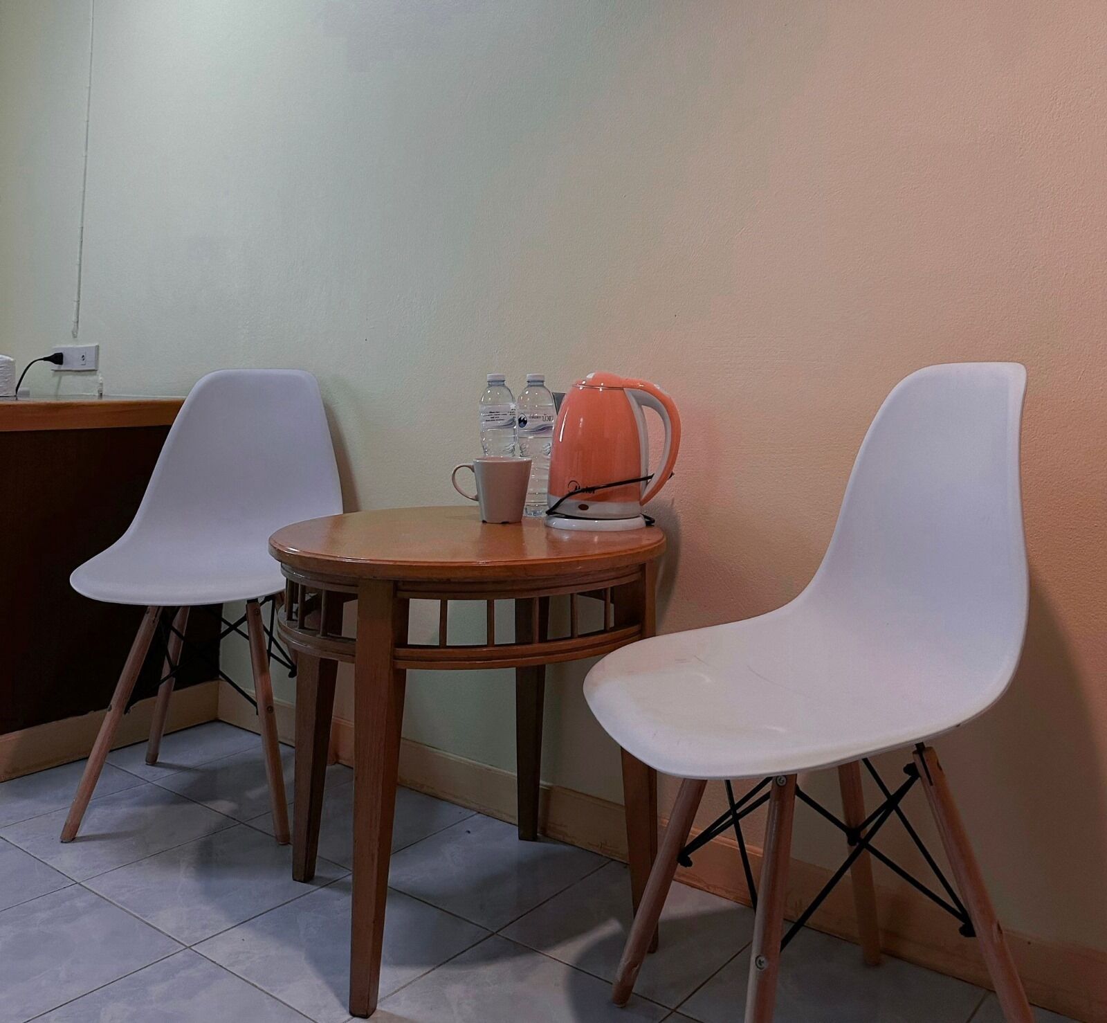 A small dining area with two white chairs, a wooden table, and a kettle.