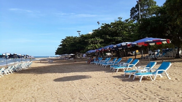 Uma praia com fileiras de espreguiçadeiras e guarda-sóis azuis e brancos, uma orla de areia e céu claro.