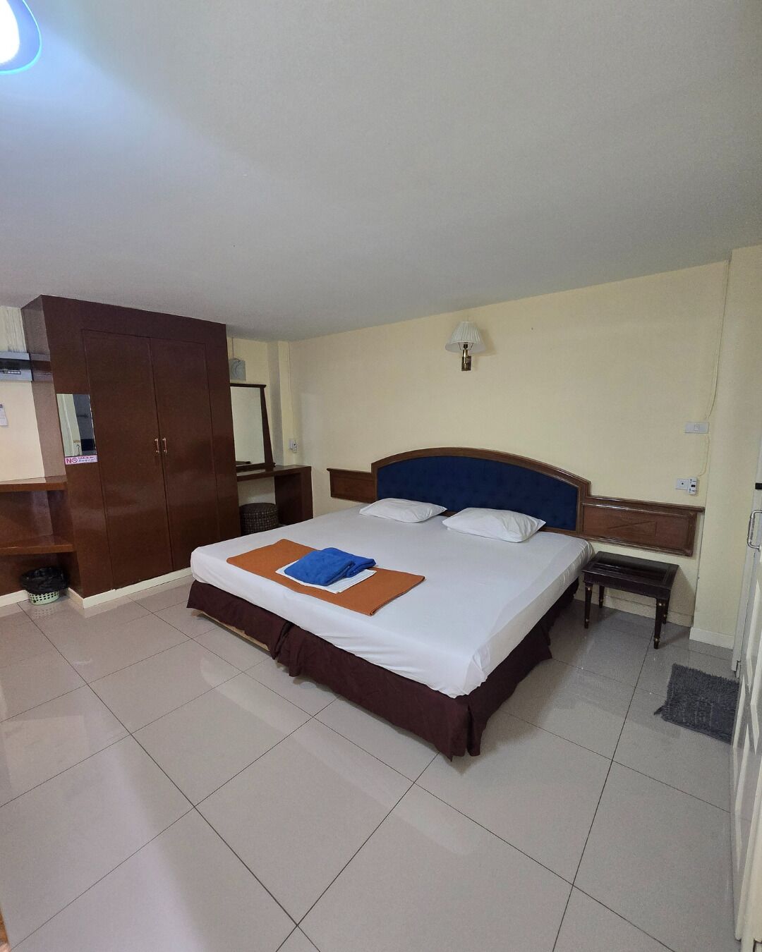 A hotel room with a large bed, a wardrobe, a nightstand, and a lamp.