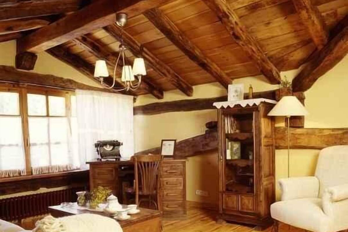 Une pièce rustique avec des poutres en bois, un fauteuil blanc, une commode en bois et un lustre.