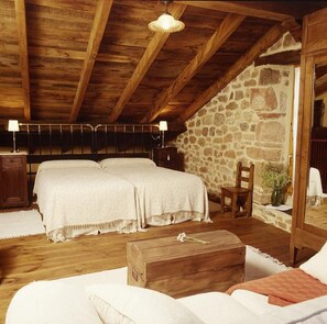 A cozy bedroom with two beds, a wooden chest, and a stone wall.