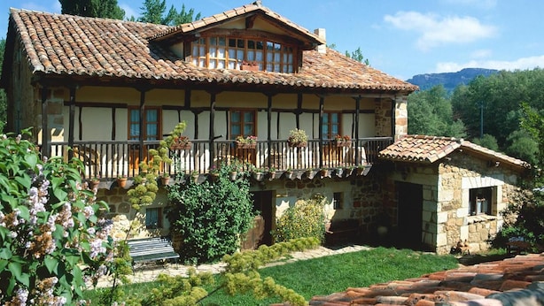 Una casa tradicional con entramado de madera y un balcón, rodeada de follaje bajo un cielo despejado.