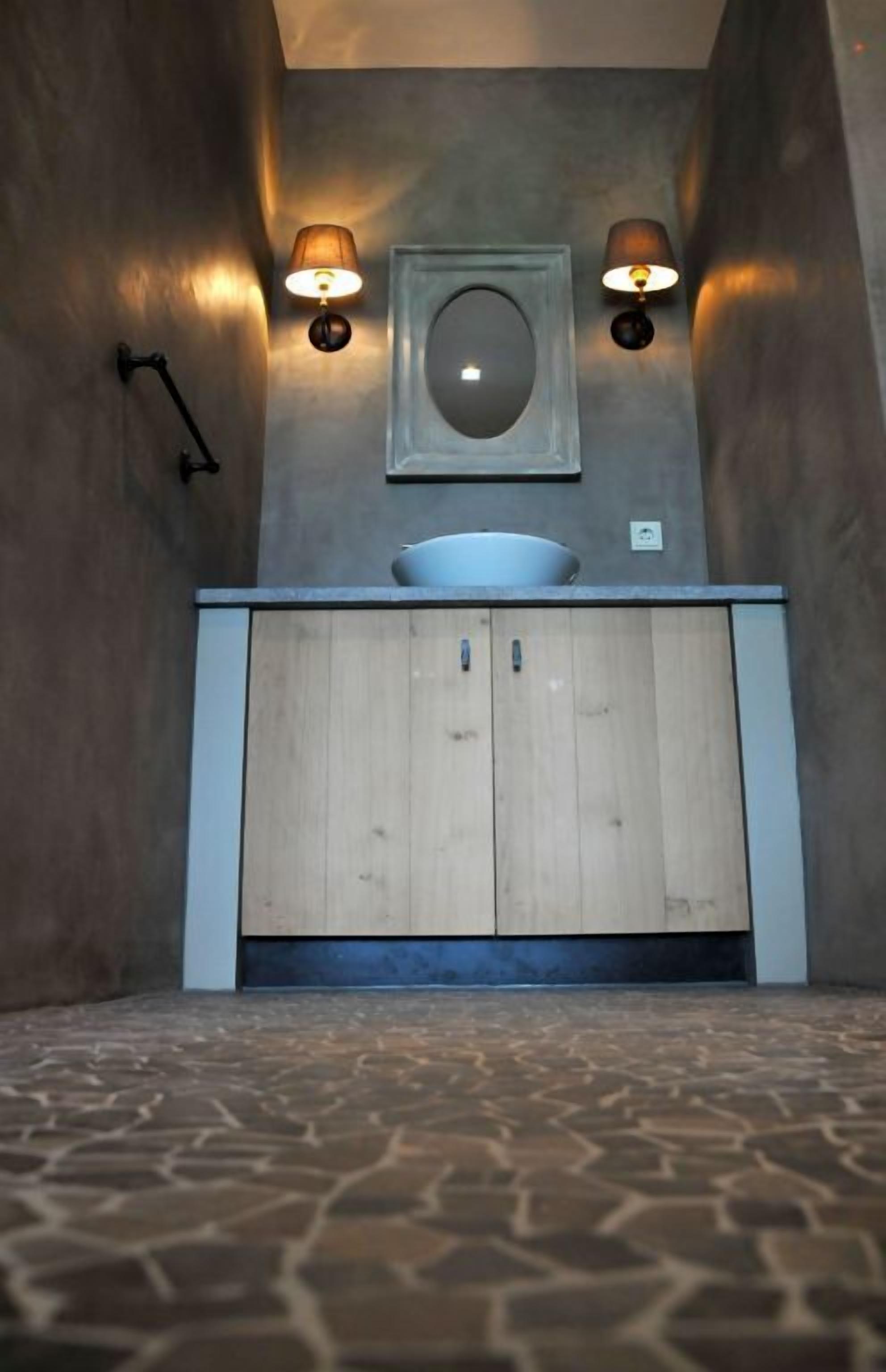 A bathroom with a wooden vanity, a round mirror, and two wall-mounted lights.