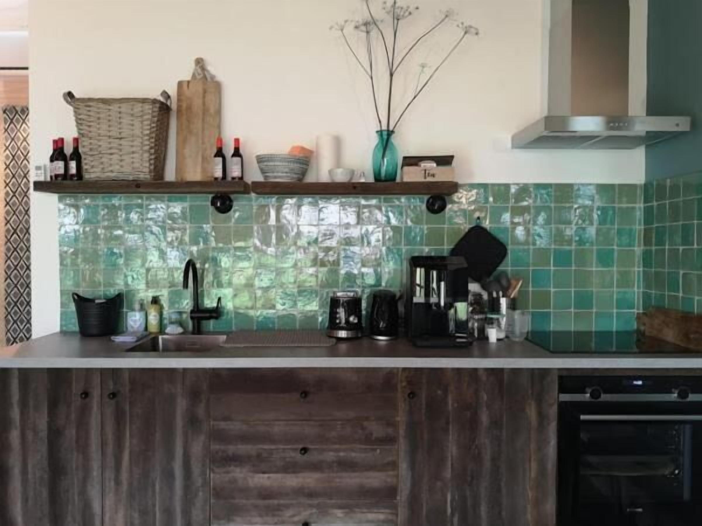 Eine Küche mit einer Holz Arbeitsplatte, einer Kaffeemaschine, einem Wasserkocher und einem Toaster. Auf der obersten Ablage stehen zwei Weinflaschen.