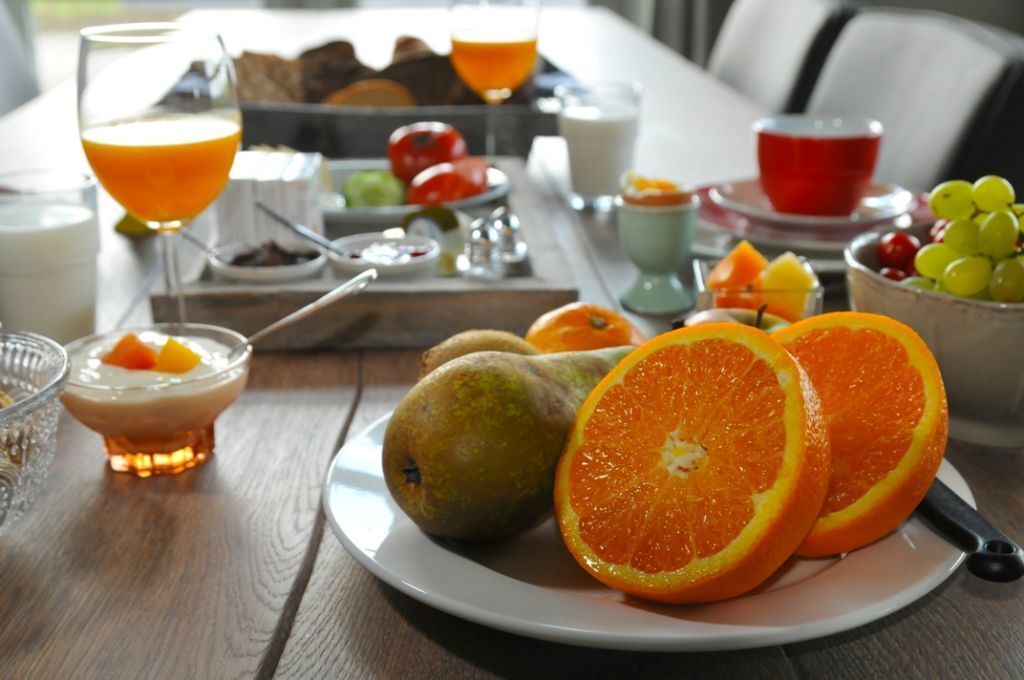 A breakfast table with fruits, a glass of orange juice, and a bowl of grapes.