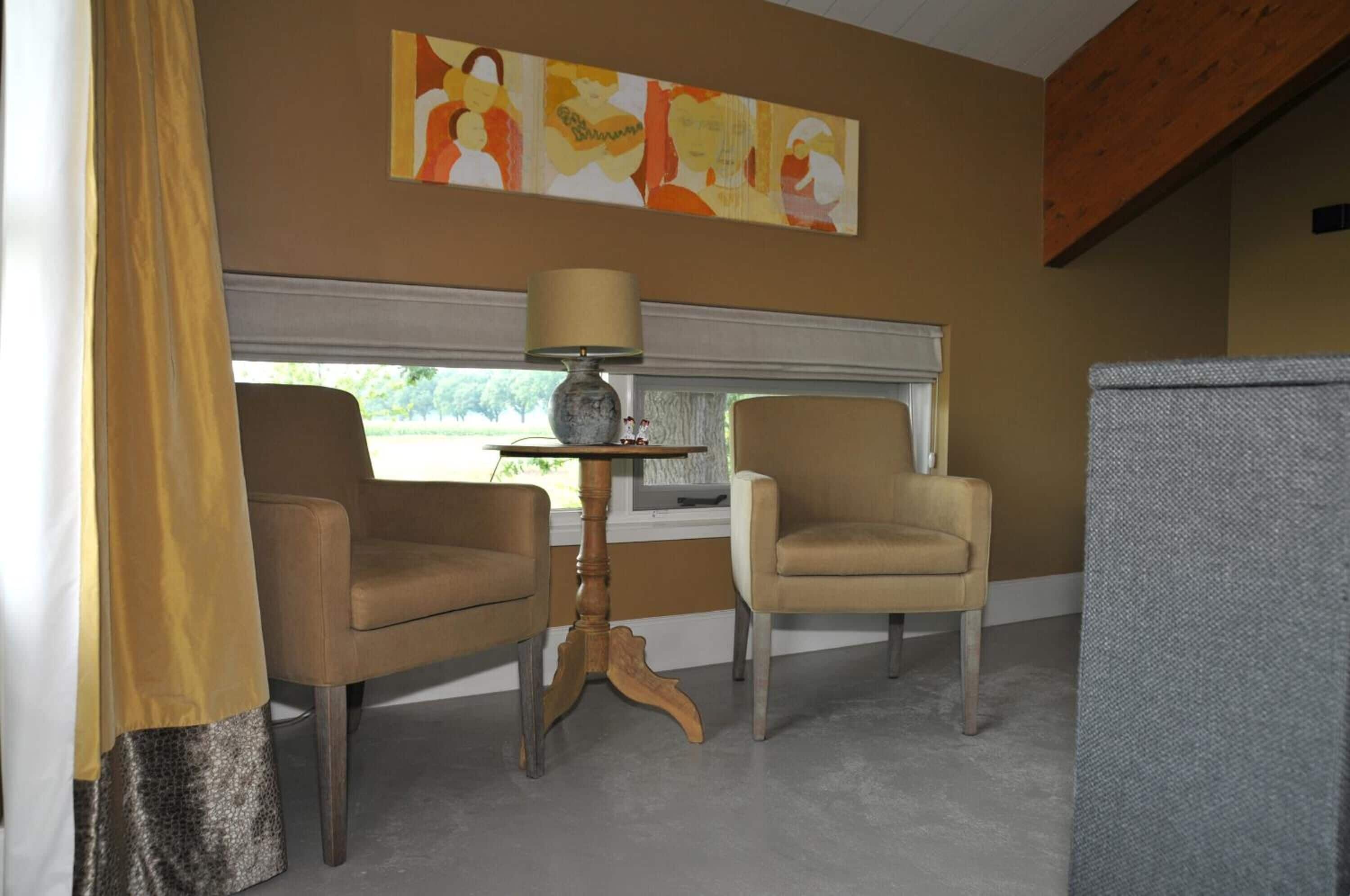 Una habitación con dos sillones, una mesita con lámpara, un cuadro abstracto grande en la pared y una ventana con persianas.