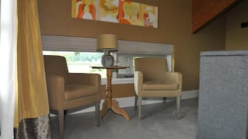 Una habitación con dos sillones, una mesita con lámpara, un cuadro abstracto grande en la pared y una ventana con persianas.