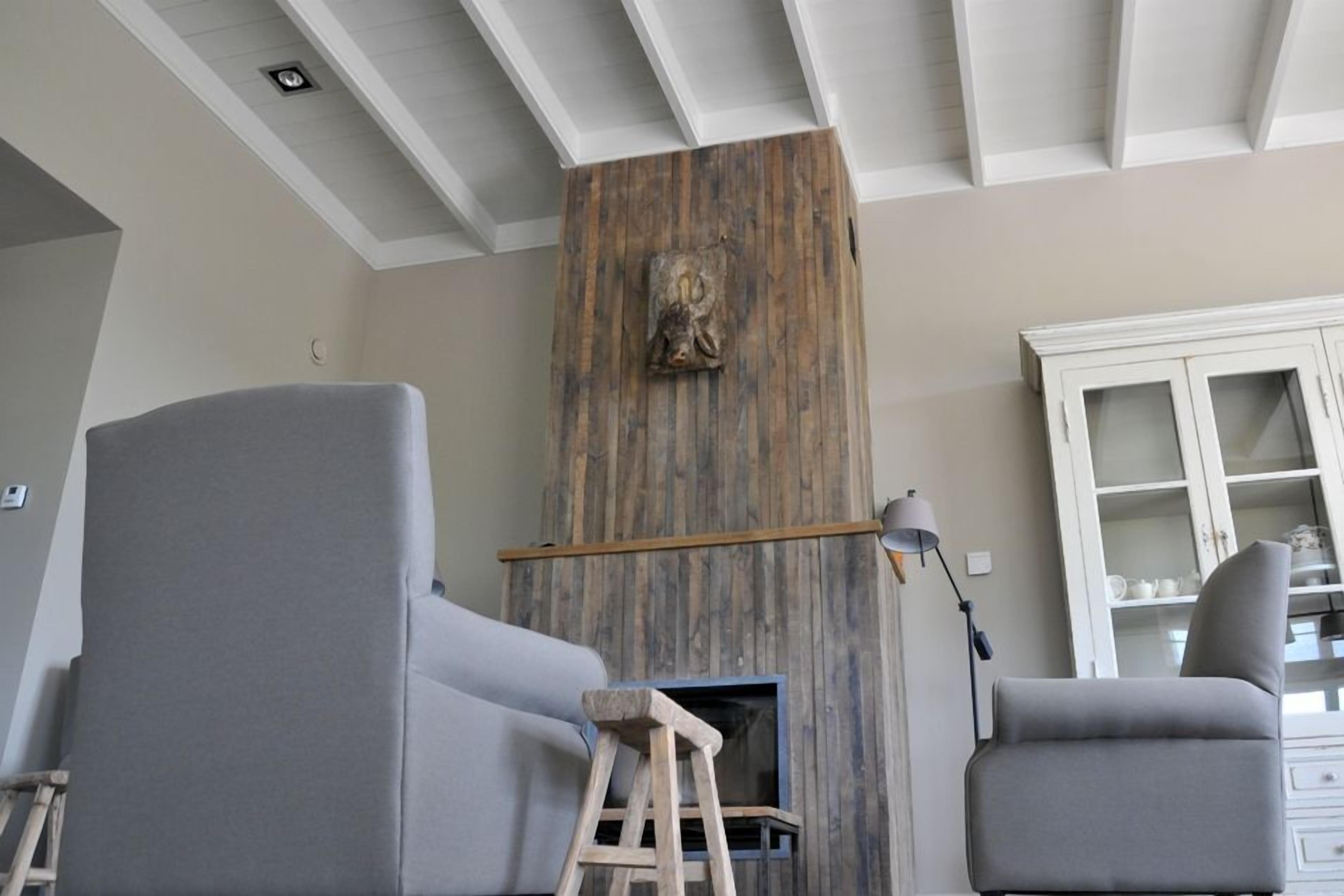 Una sala de estar con dos sofás grises, una escalera de madera y una chimenea con pared rústica.
