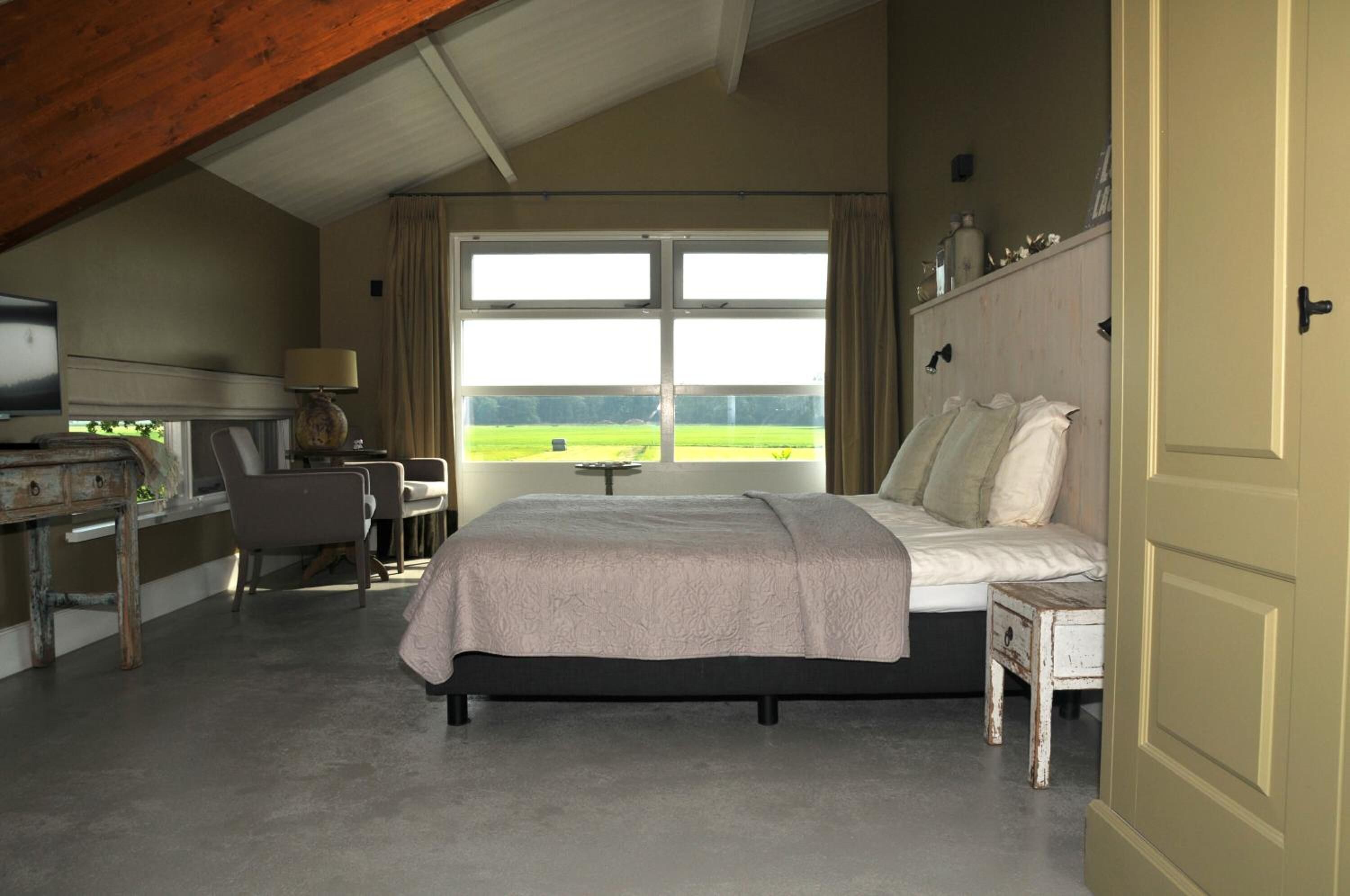 Un dormitorio con cama, escritorio, silla y un ventanal con vistas a un campo verde.