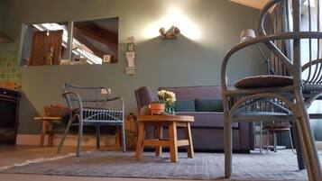 A cozy living room with a sofa, two chairs, a small table with a vase, and a staircase.