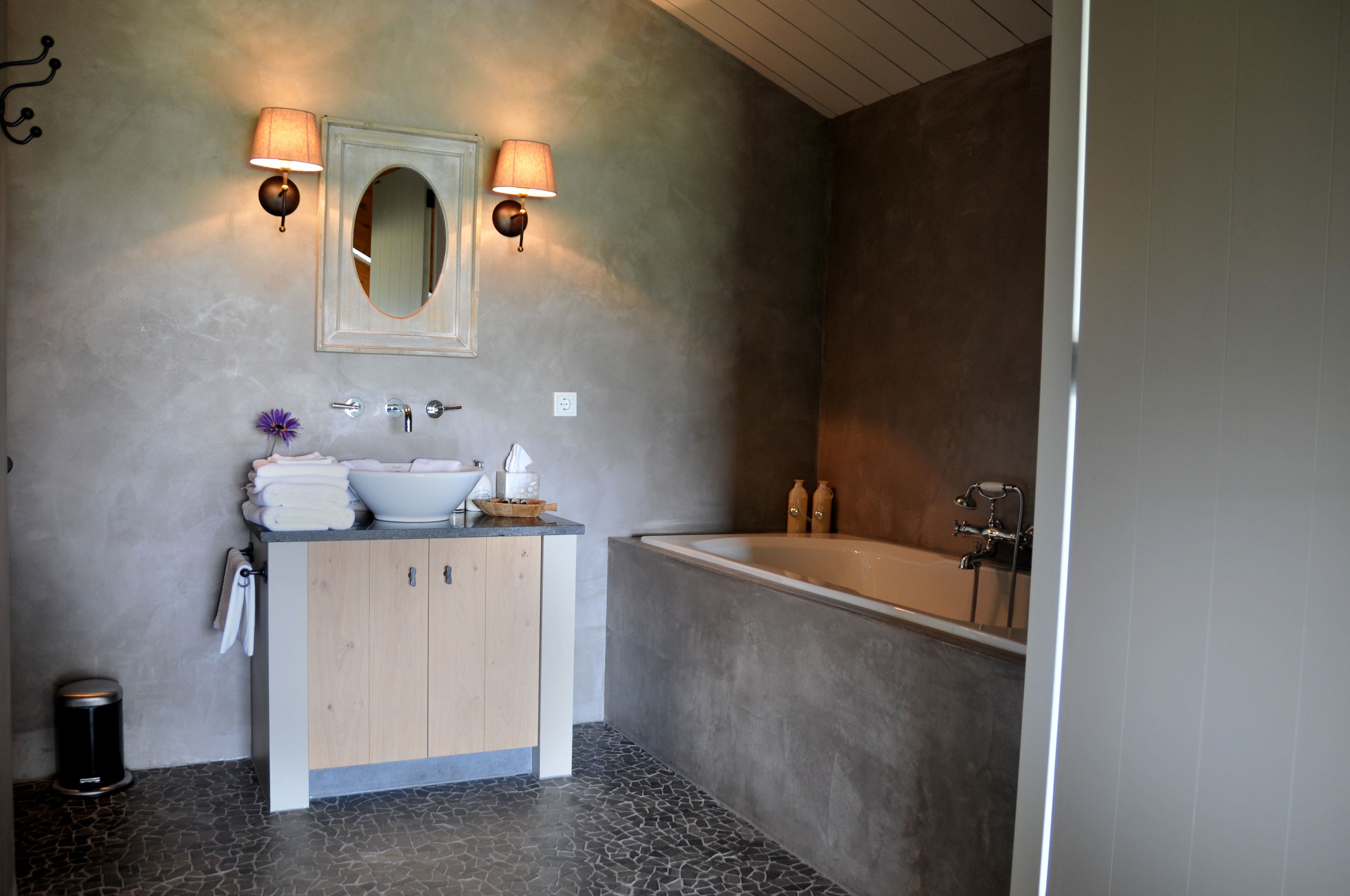 A modern bathroom with a freestanding bathtub, a vanity with a mirror and two wall-mounted lamps, and a small sink.