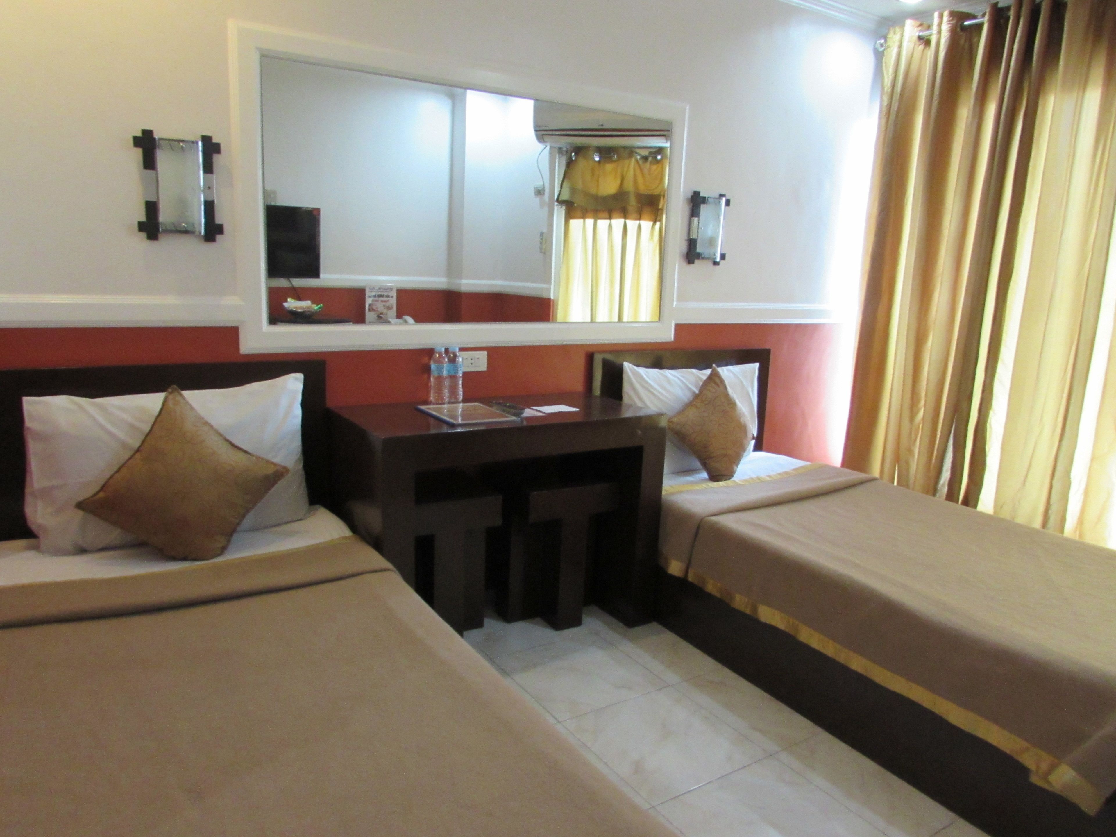 A hotel room with two single beds, a small desk, a mirror, and a window with curtains.