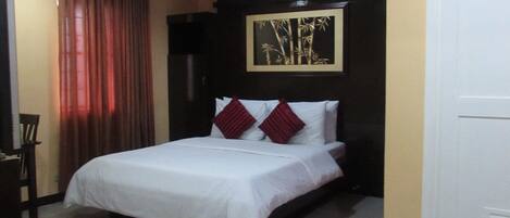 A hotel room with a bed, a chair, a desk, and a door.