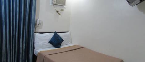 Una habitación pequeña con cama individual, una cortina azul, aire acondicionado instalado en la pared y un televisor.