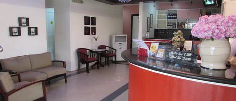 A reception area with a red counter, a clock on the wall, and a TV screen displaying a program.