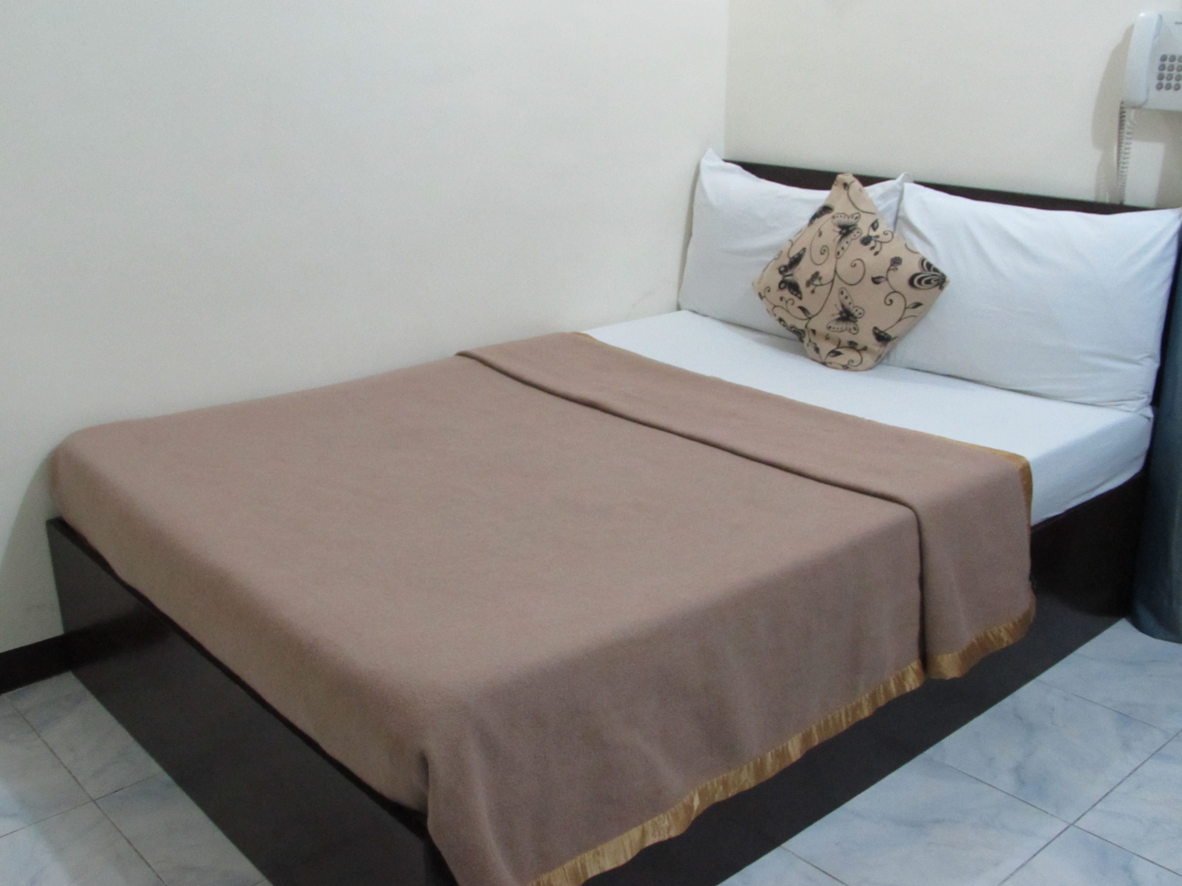 A single bed with a beige blanket, white pillows, and a patterned pillow.