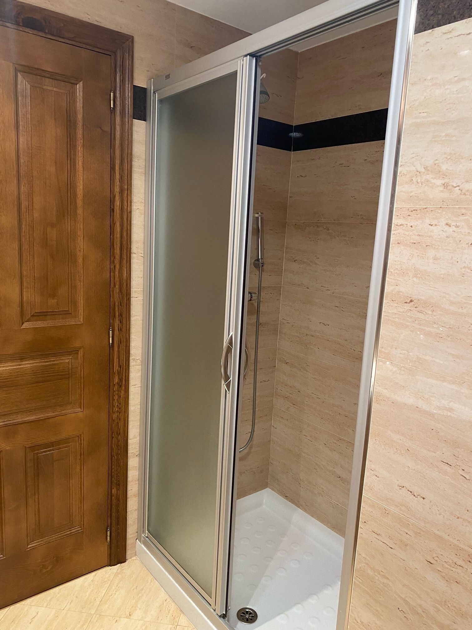A walk-in shower with a glass door, wooden door frame, and tiled floor.