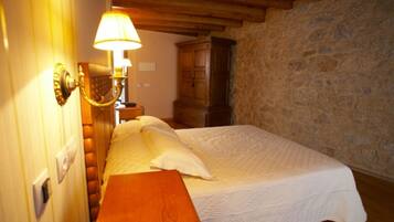 Un dormitorio con cama de madera, mesita de noche, lámpara y pared de piedra.