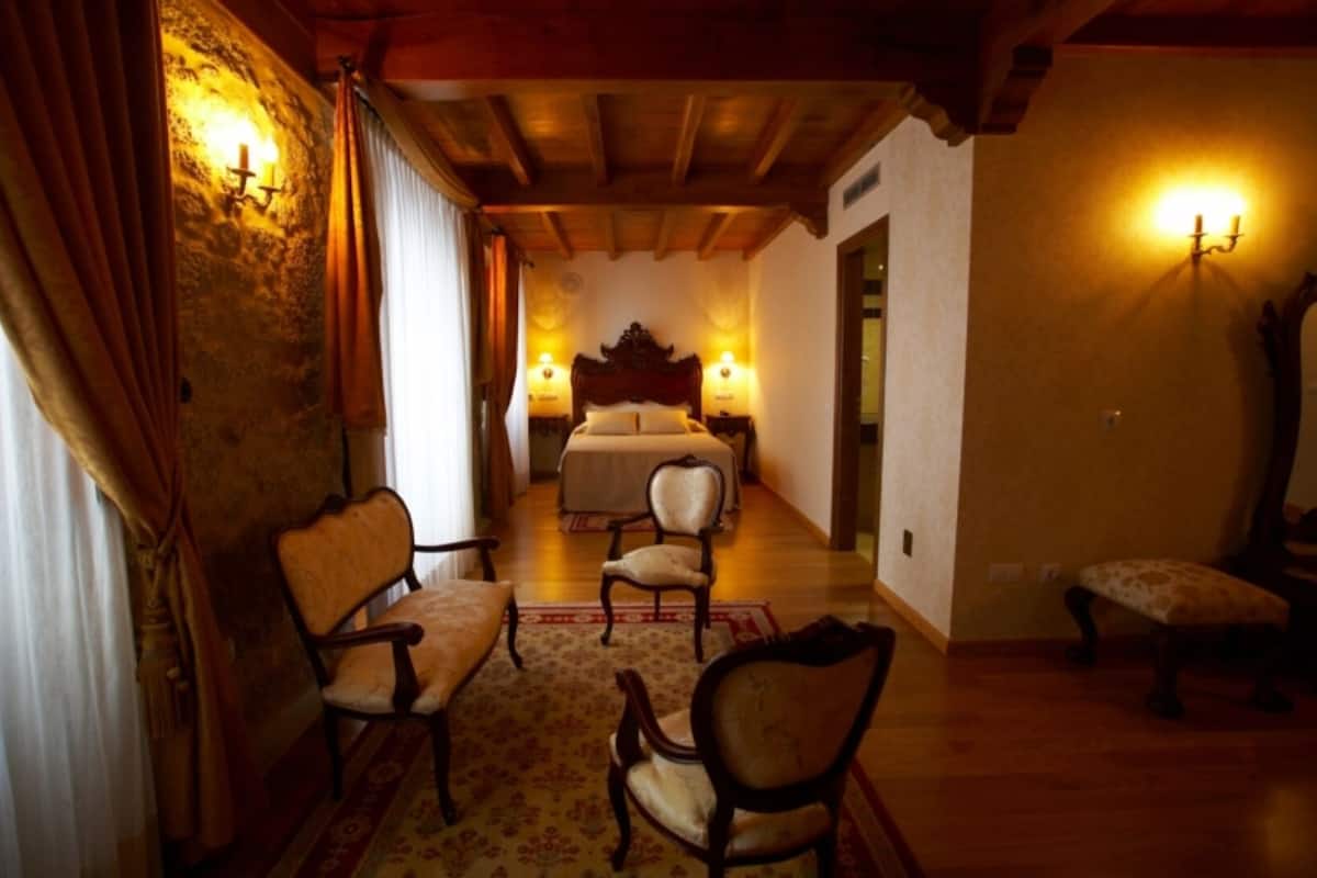 A room with a bed, two chairs, a wooden floor, and a stone wall.