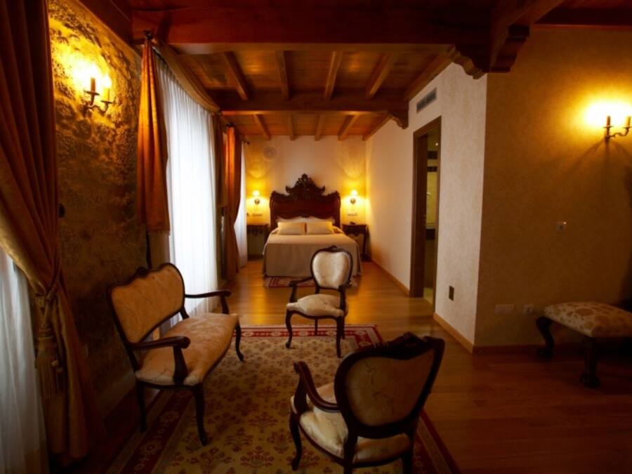 A room with a bed, two chairs, a wooden floor, and a stone wall.