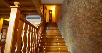 Una escalera de madera con barandilla que conduce a un rellano con un reloj y una pared de superficie texturizada.