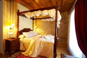 Ein Himmelsbett mit Baldachin, ein Nachttisch mit Lampe und eine Wand aus Stein im Hintergrund.
