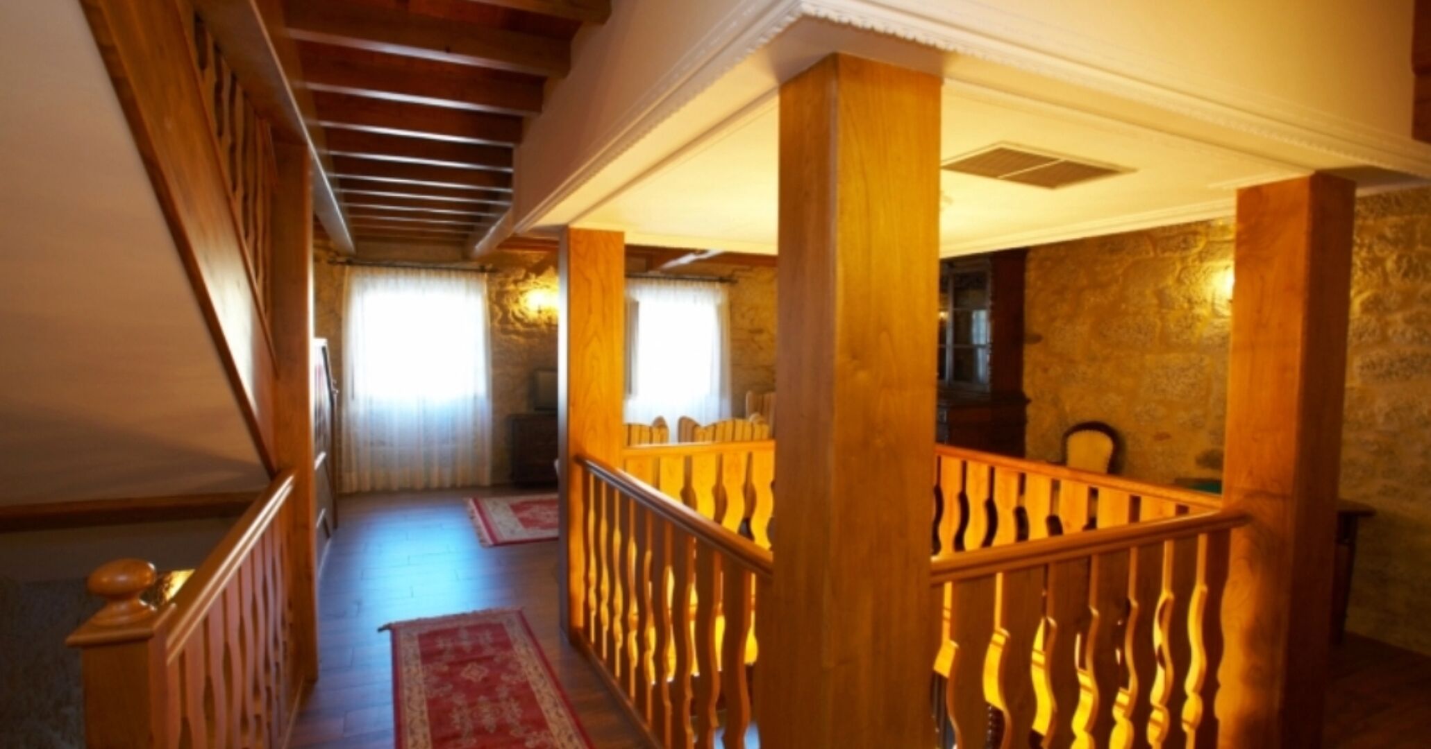 Un escalier en bois recouvert d’une moquette rouge mène à une pièce aux murs de pierre et dotée d’une fenêtre avec des rideaux.
