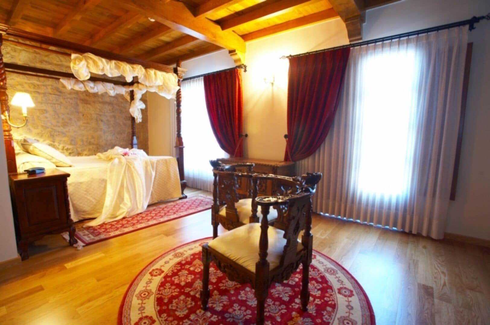 Una habitación con una cama, una silla de madera, una mesa y un tapete de diseño rojo y blanco.