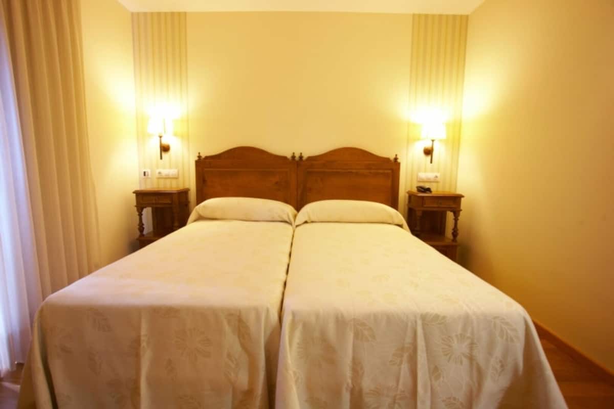 A double bed with a wooden headboard, two bedside tables with lamps, and a window with curtains.