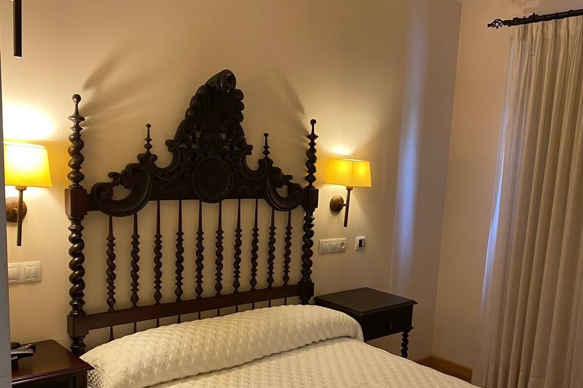 A neatly made bed with a wooden headboard, two bedside lamps, and a nightstand with a lamp.