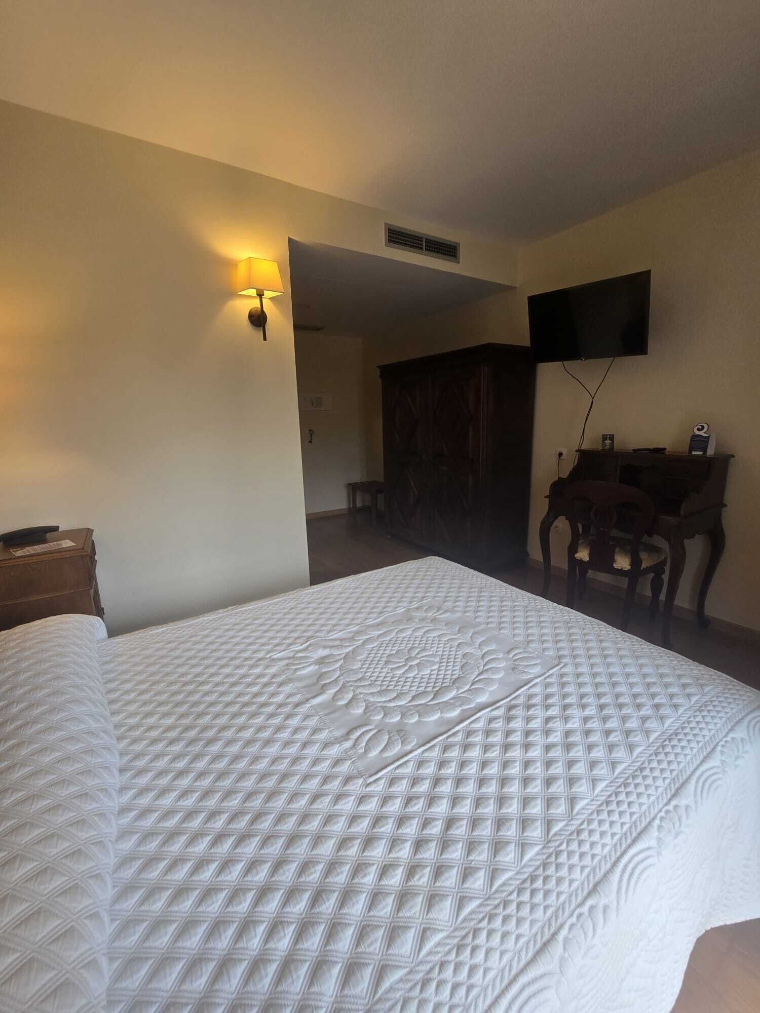 A hotel room with a large bed, a desk with a chair, a television mounted on the wall, and a wardrobe.