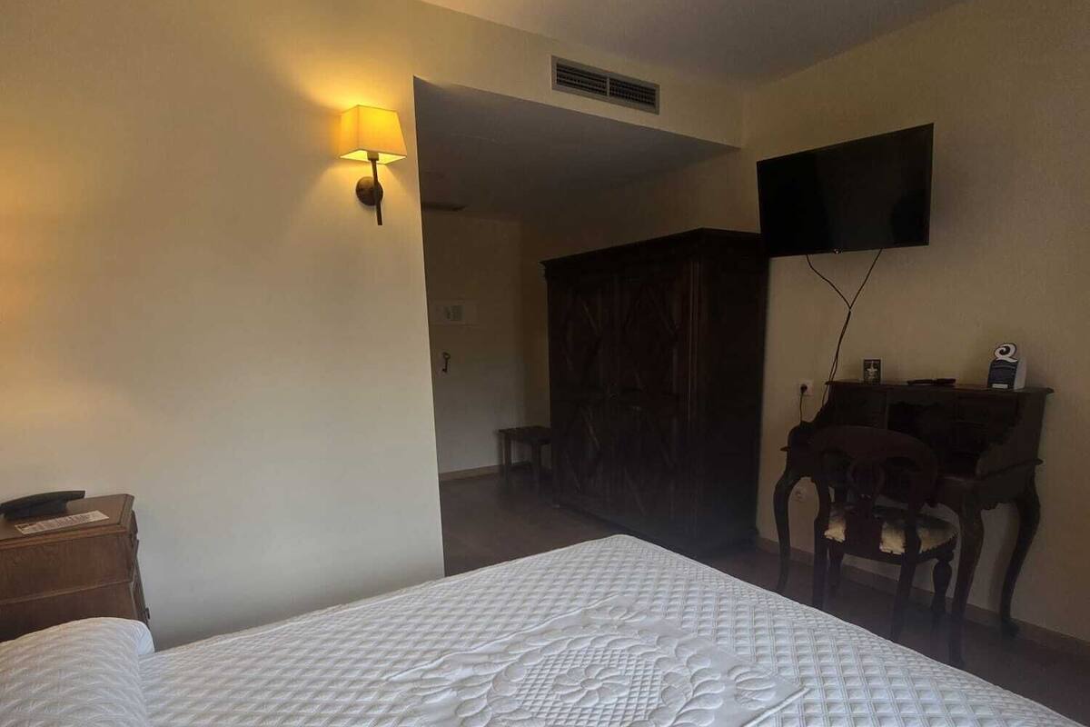 A hotel room with a large bed, a desk with a chair, a television mounted on the wall, and a wardrobe.