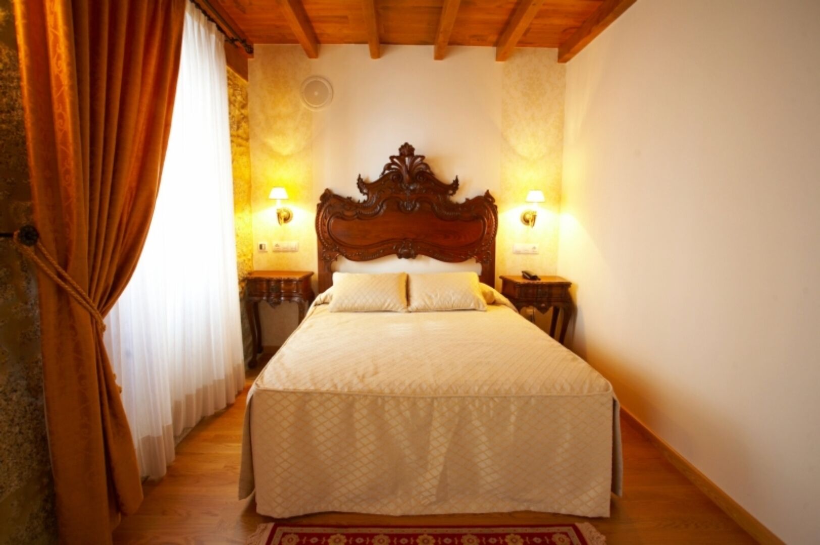 A bedroom with a large bed, wooden headboard, two bedside tables with lamps, and a wooden floor.
