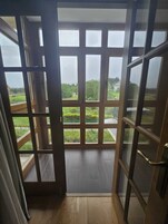 Una habitación con un ventanal grande, piso de madera y vistas a zonas verdes.