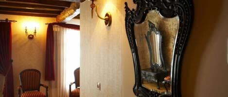 A room with a wooden ceiling, a red and white patterned chair, a wall-mounted lamp, and a large ornate mirror.