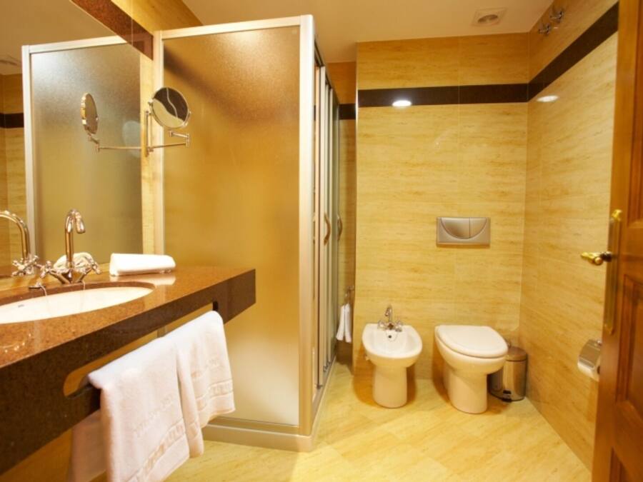 Un baño moderno con un lavamanos grande, un espejo, una ducha y dos inodoros.