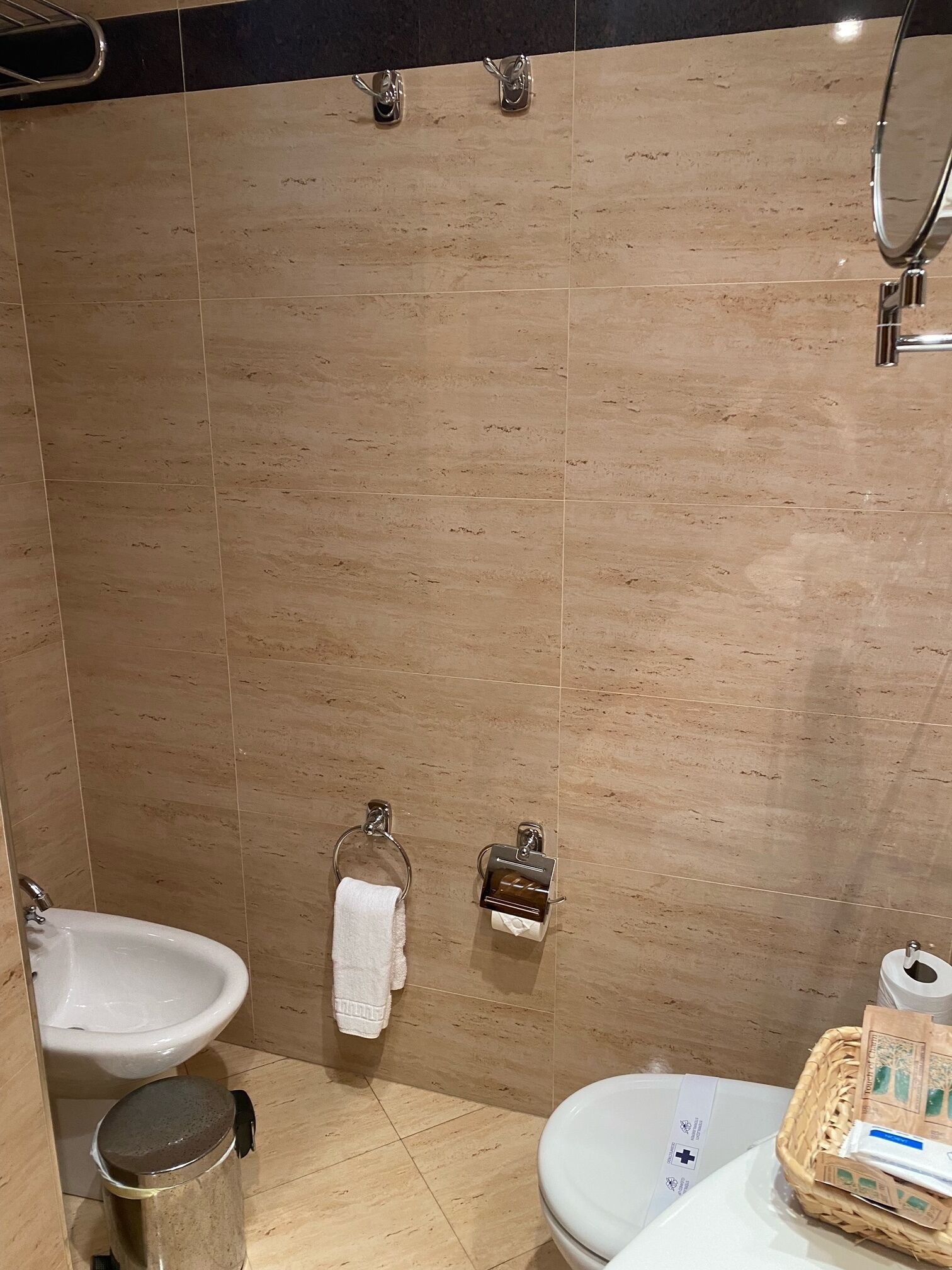 Un baño con baldosas color beige, un lavamanos, un inodoro, un bidé y un cubo de basura.