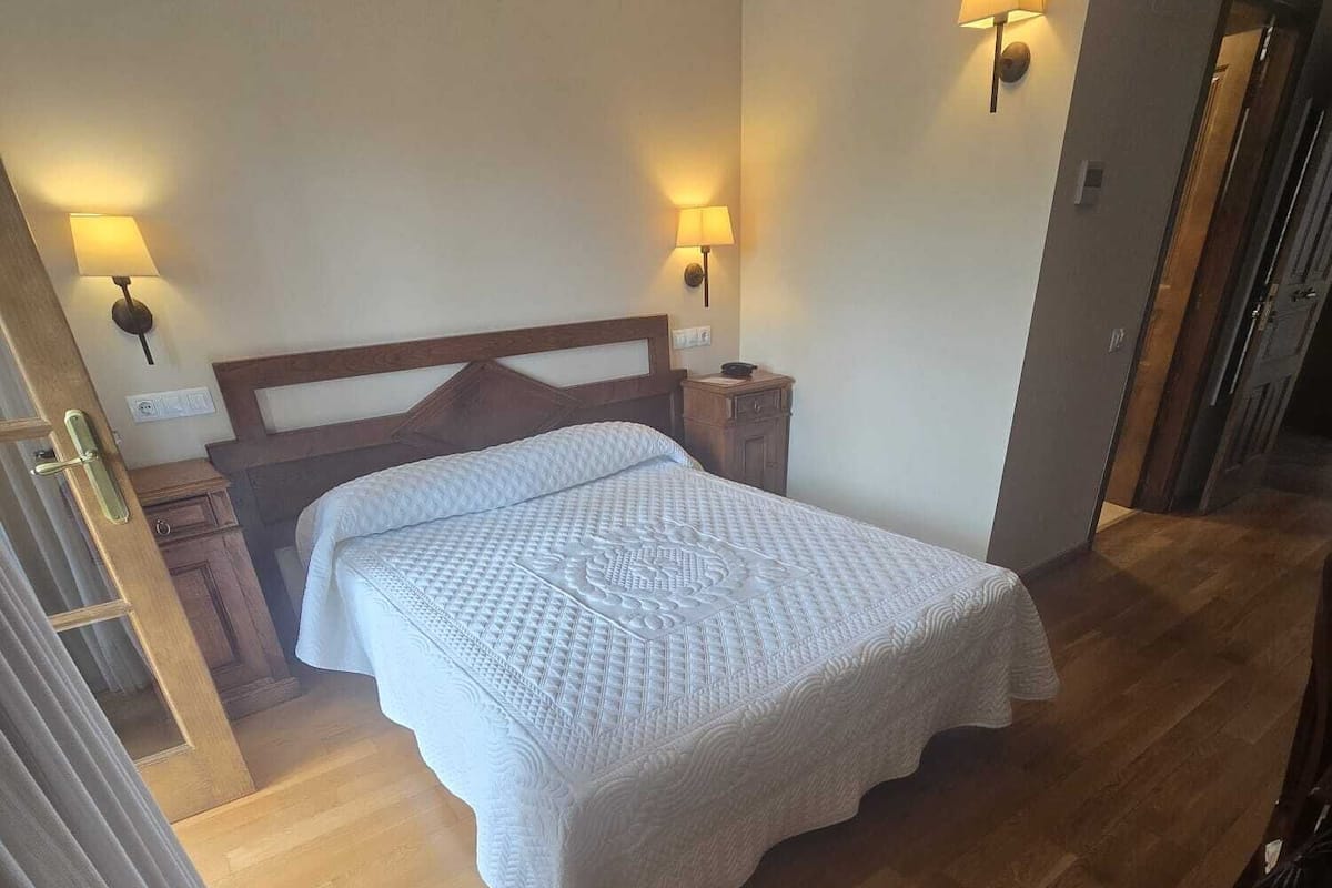 A bedroom with a wooden bed, two bedside lamps, a nightstand, and a wooden floor.
