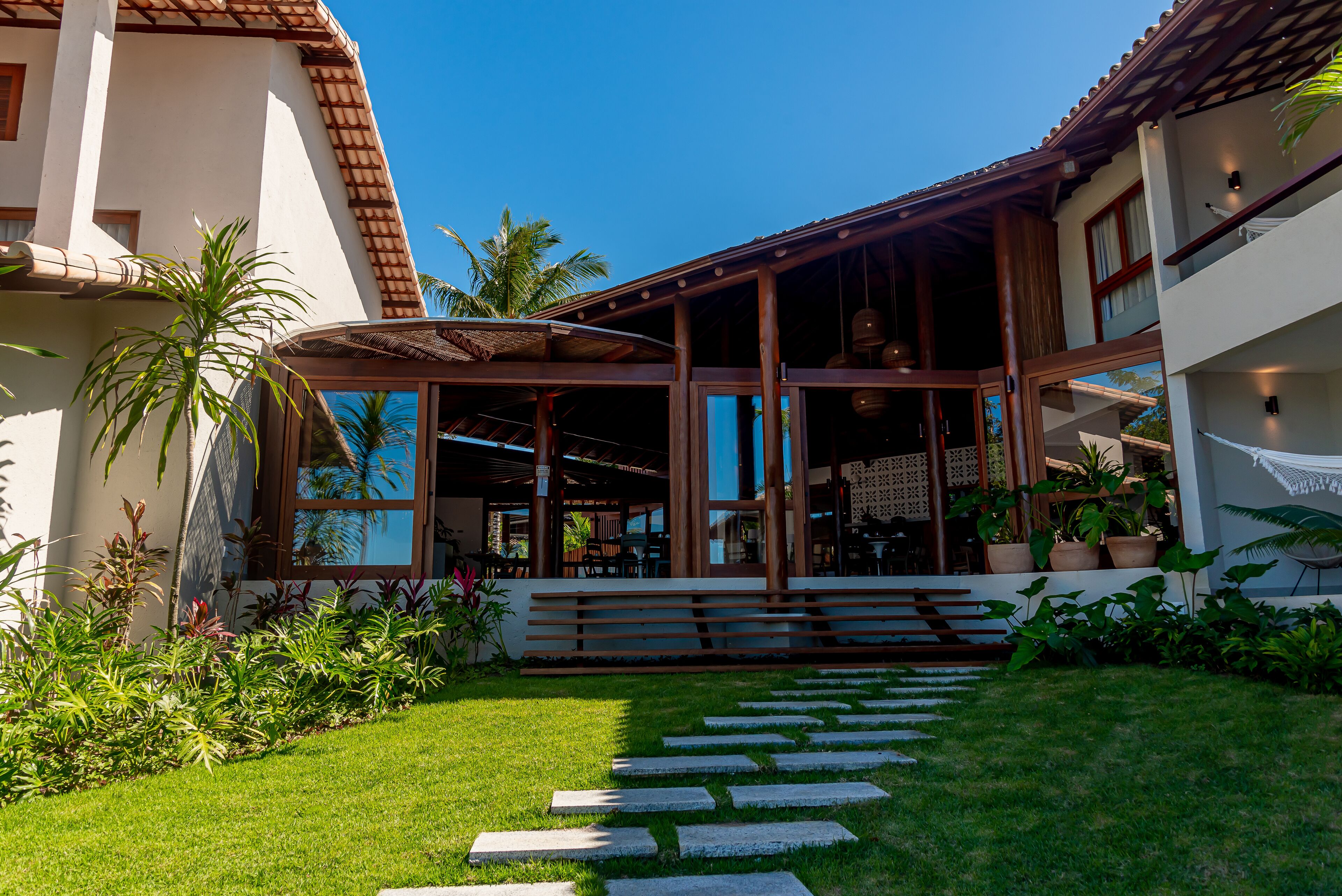 A modern house with a covered patio, a stone pathway, and lush greenery.