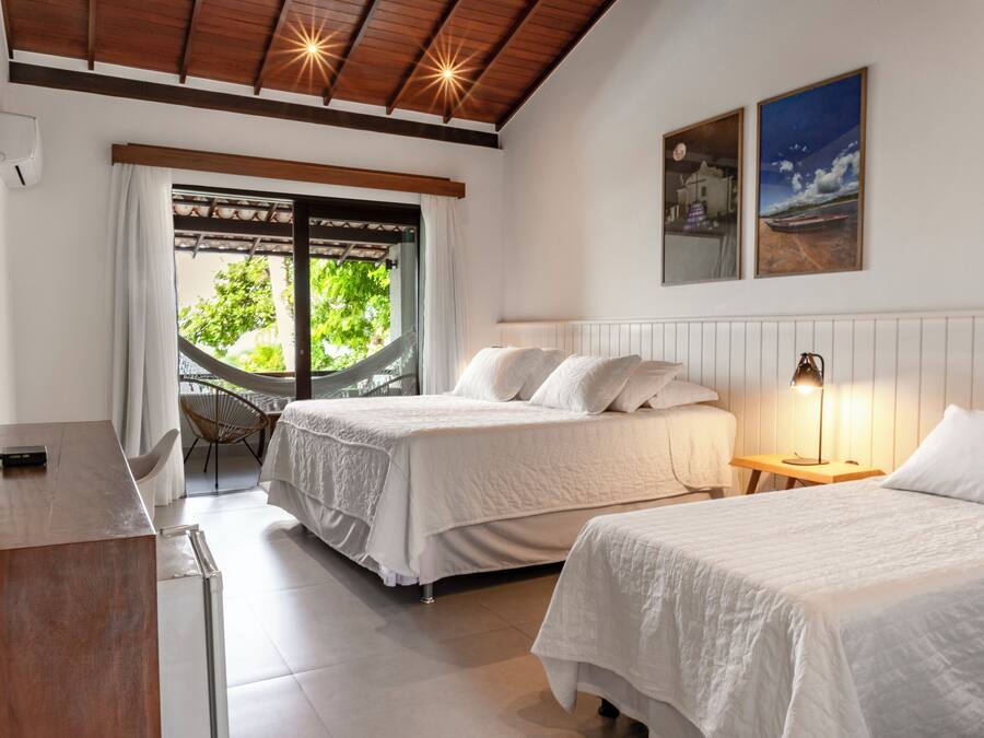 A hotel room with two beds, a desk, a chair, a hammock, and a view of greenery outside.