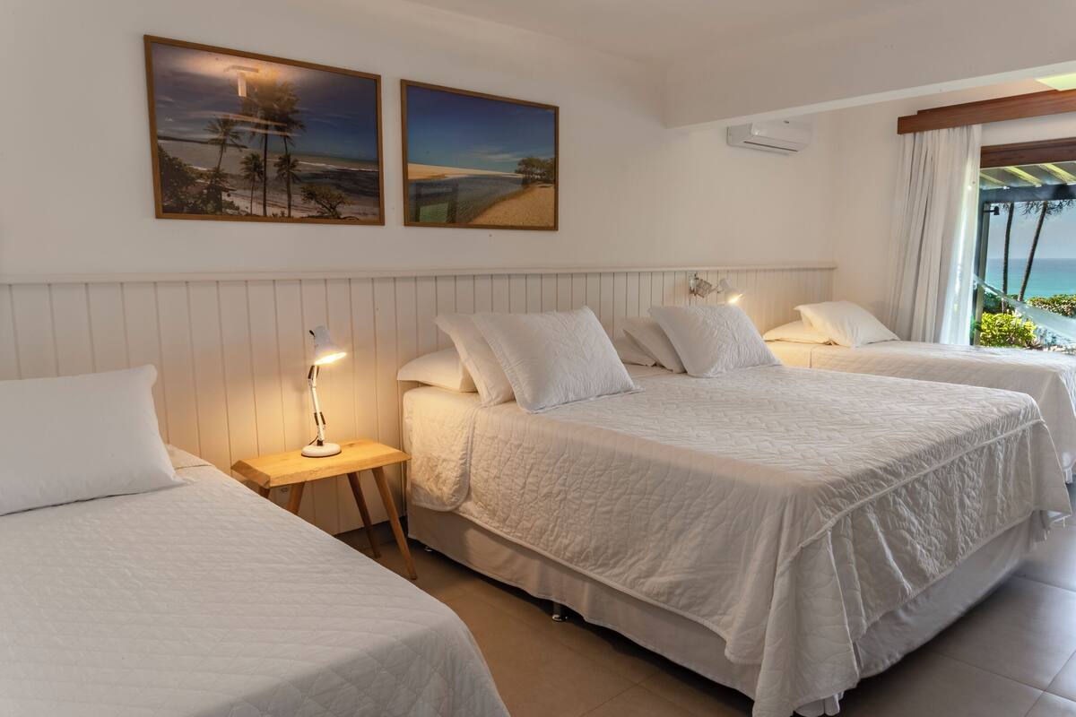 A hotel room with two beds, a nightstand with a lamp, and a view of the ocean.
