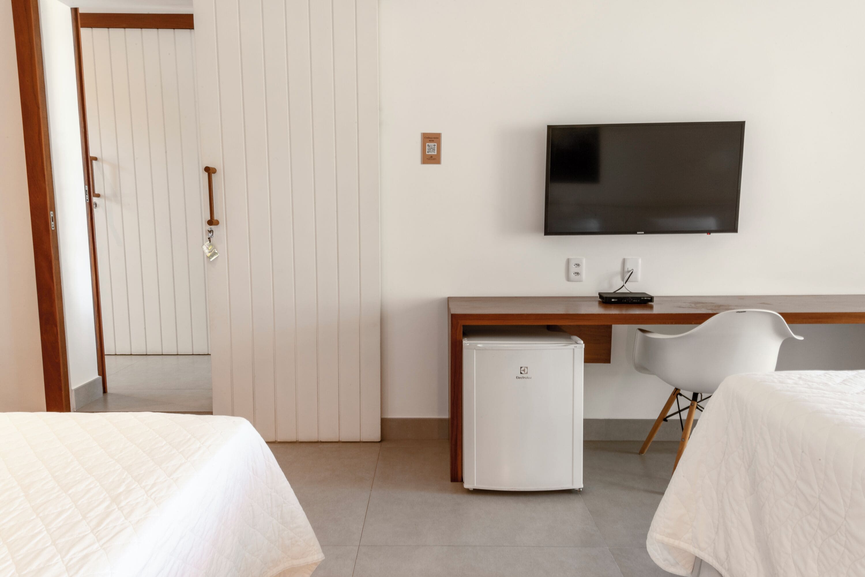 A hotel room with a bed, a desk, a television, and a refrigerator.