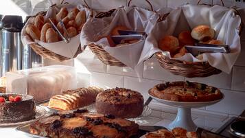 A buffet table with various baked goods, cakes, and a pie.