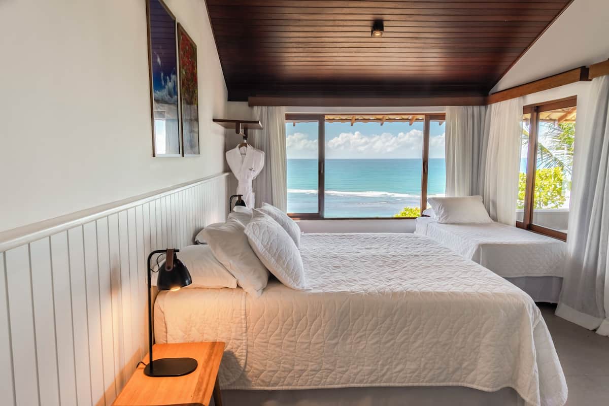 A bedroom with two beds, a nightstand, and a view of the ocean.
