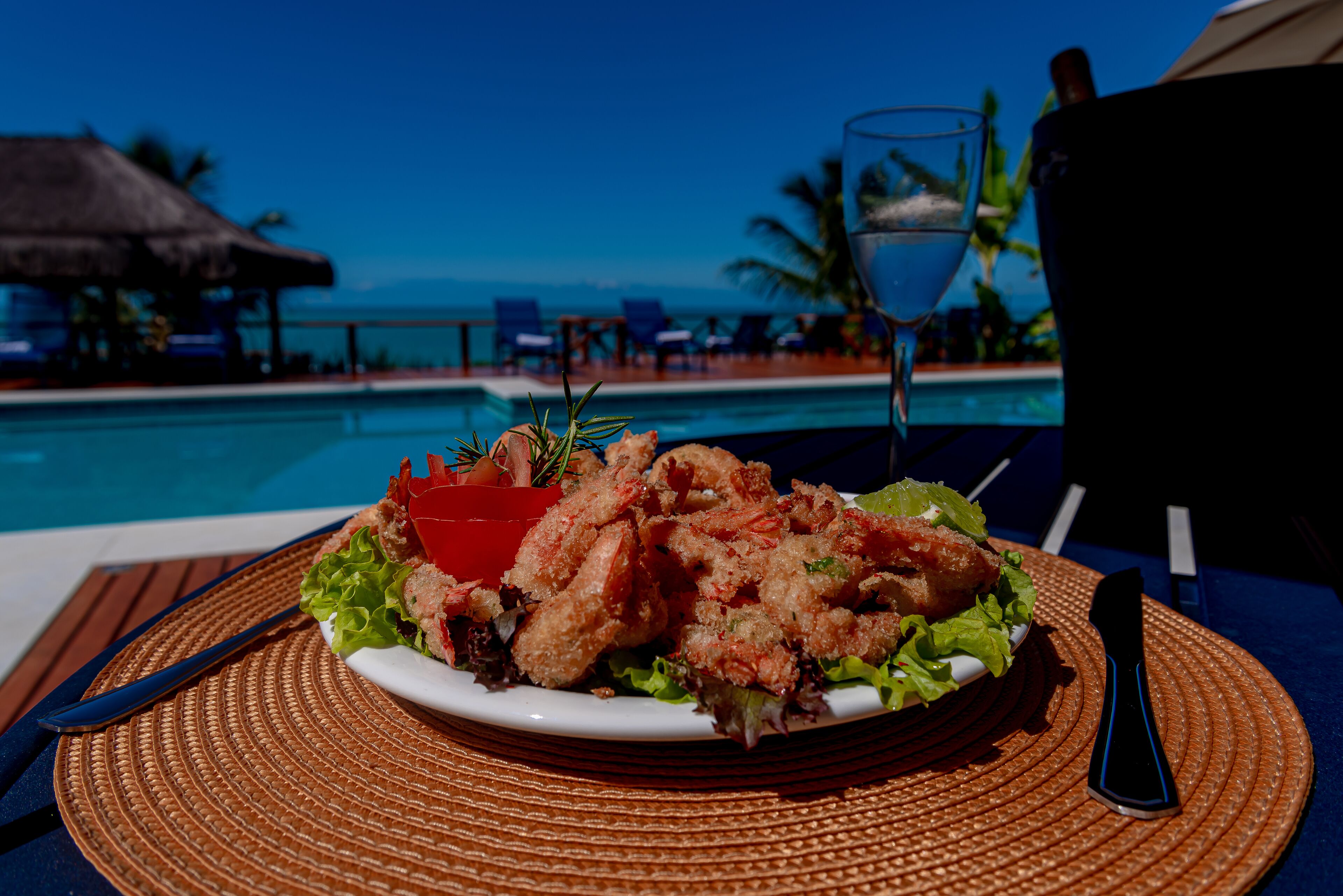 A plate of seafood on a table by a pool with a view of the ocean.