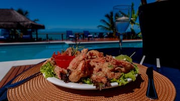 Prato de mariscos em uma mesa perto de uma piscina, com vista para o oceano.