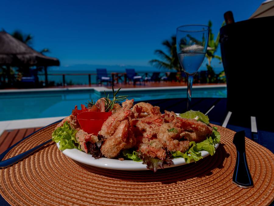 Prato de mariscos em uma mesa perto de uma piscina, com vista para o oceano.
