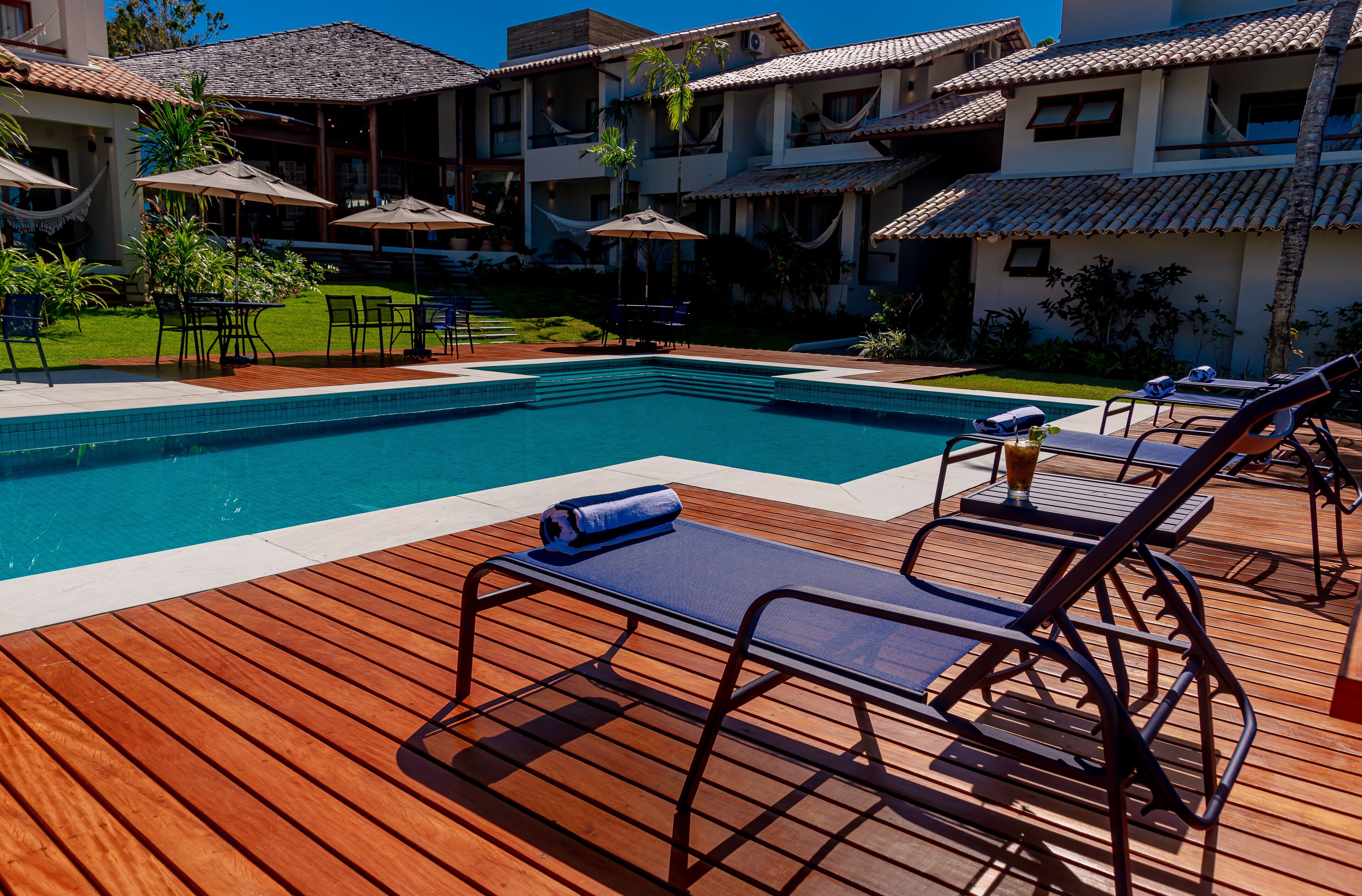 A pool area with wooden deck, lounge chairs, and umbrellas.