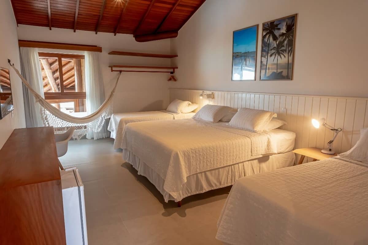 A room with two beds, a hammock, wooden beams, and a view of the beach.